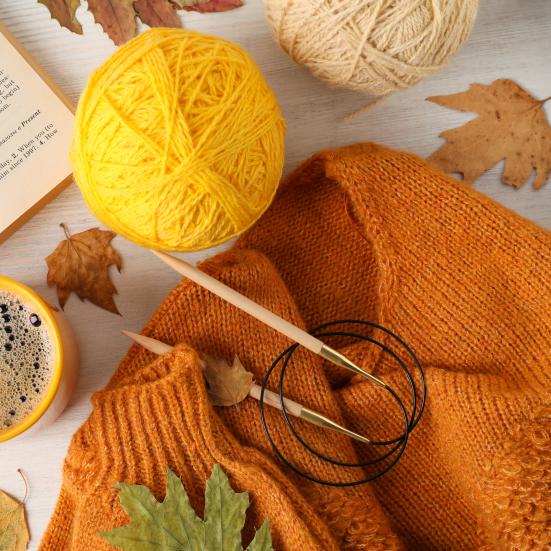 En orange striktrøje, strikkepinde og gult garn.
