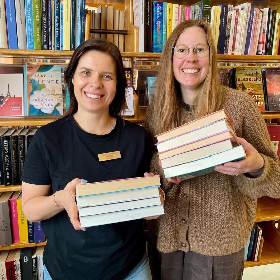 Bibliotekarer Marianne Wismar Mühring og Johanne Søndergaard Louv står med hver deres bogstak og smiler.