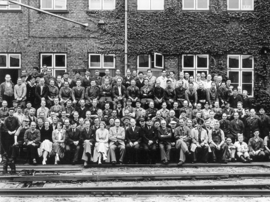 Personalet ved DSB Værksted Nyborg opstillet til fotografering. I baggrunden værkstedets administrations- og lagerbygning. 1951.